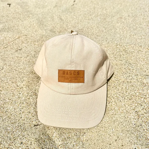 Casquette beige BASCS posée sur le sable de la plage.